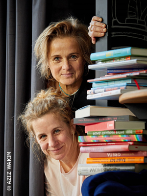 Kuratorinnen Ilona Einwohlt und Meike Heinigk schauen hinter Büchern hervor